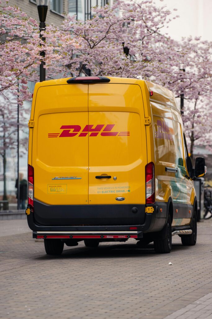 Yellow DHL van parked on a blossom-lined street in Jönköping, Sweden.